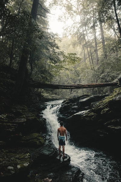 站在瀑布边的一个身穿青色和黑色短裤的男人